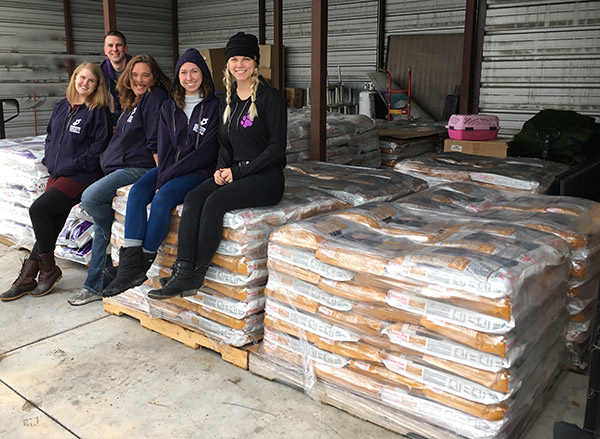 FABFAS Donation photo: five volunteers pose with pet food bags on pallets